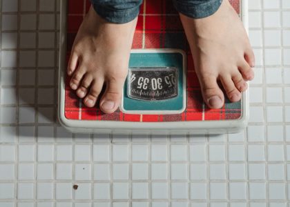 From above crop anonymous barefoot child in jeans standing on weigh scales on tiled floor of bathroom