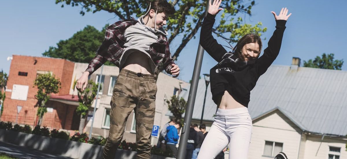 Two teenagers joyfully jumping outdoors in Šiluva, Lithuania under a bright blue sky. Captured in springtime.