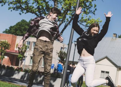 Two teenagers joyfully jumping outdoors in Šiluva, Lithuania under a bright blue sky. Captured in springtime.