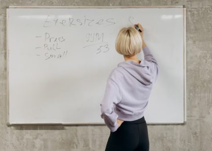 Female writing workout schedule on whiteboard in gym setting.